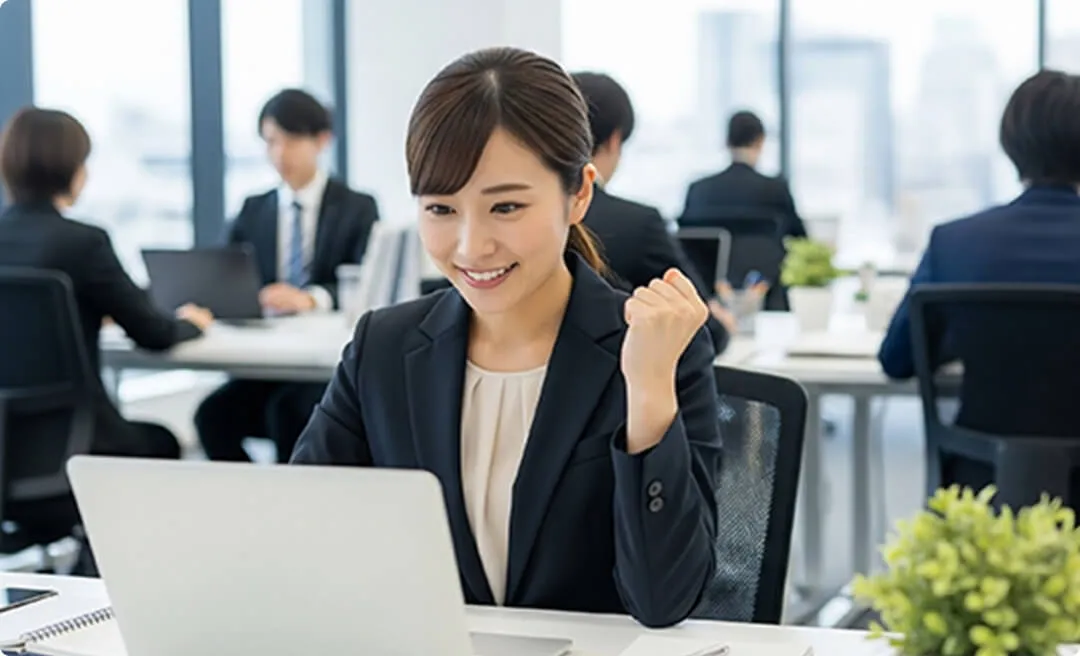 パソコンの画面を見ながらガッツポーズをしている女性従業員の画像